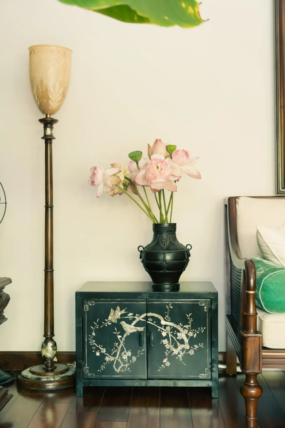 Pink lotus flowers in a dark bronze vase on a black lacquer cabinet beside a brass lamp.