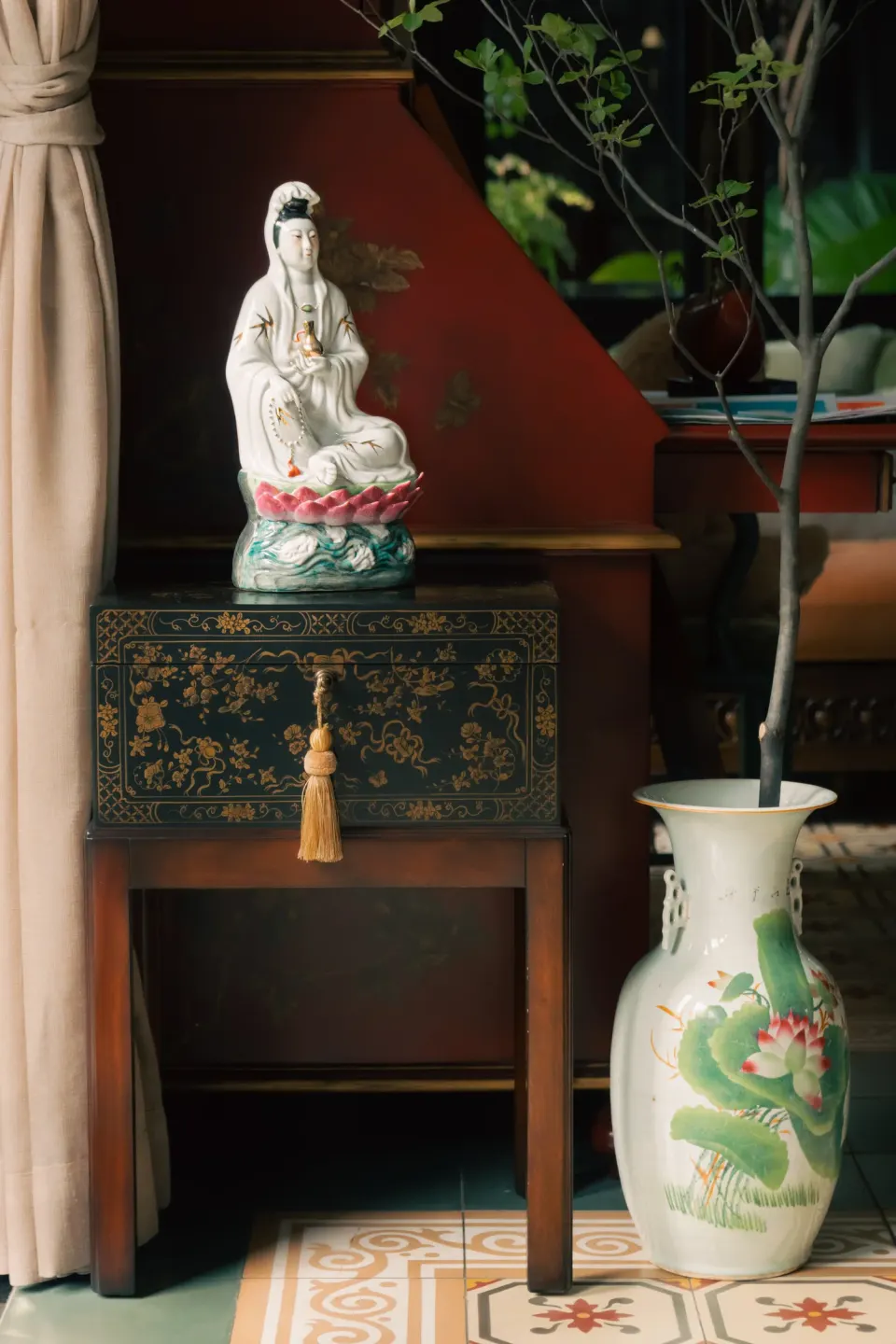 A porcelain Guanyin on a lacquer chest beside a tall green-glazed vase.