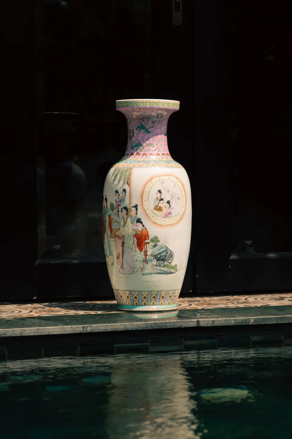 A tall painted vase with figures on the edge of a pool.