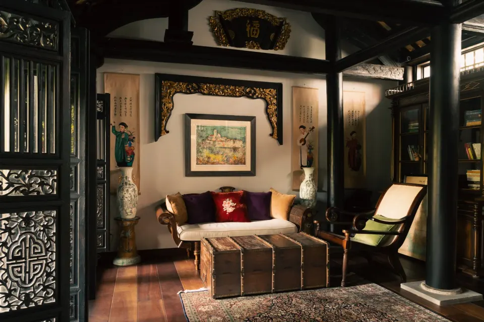 A dark-wood Indochine villa sitting room with carved screens, a framed painting and a daybed.