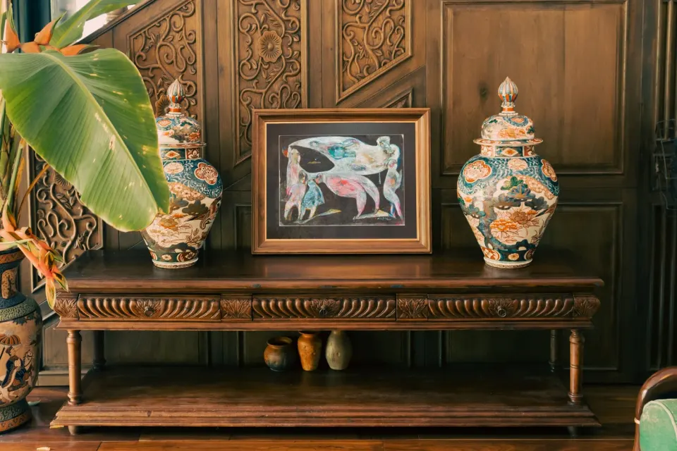 A carved wooden console with two lidded vases and a framed painting of figures.