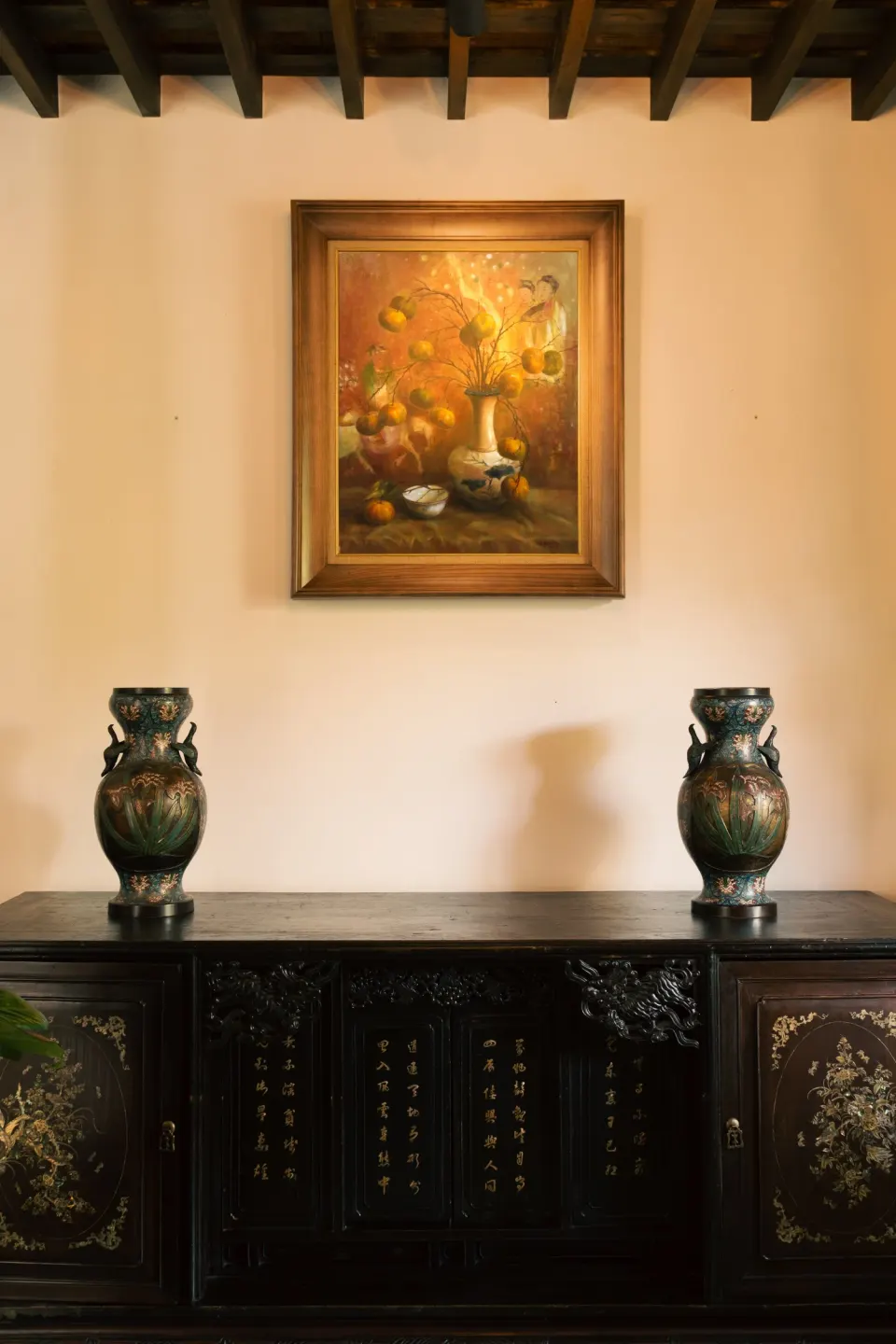 A framed painting above a dark console with two bronze vases.