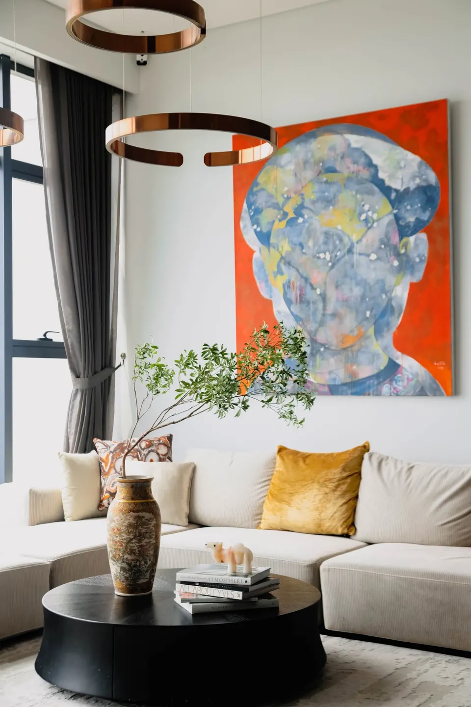 A living room with a large orange portrait painting above a cream sofa.