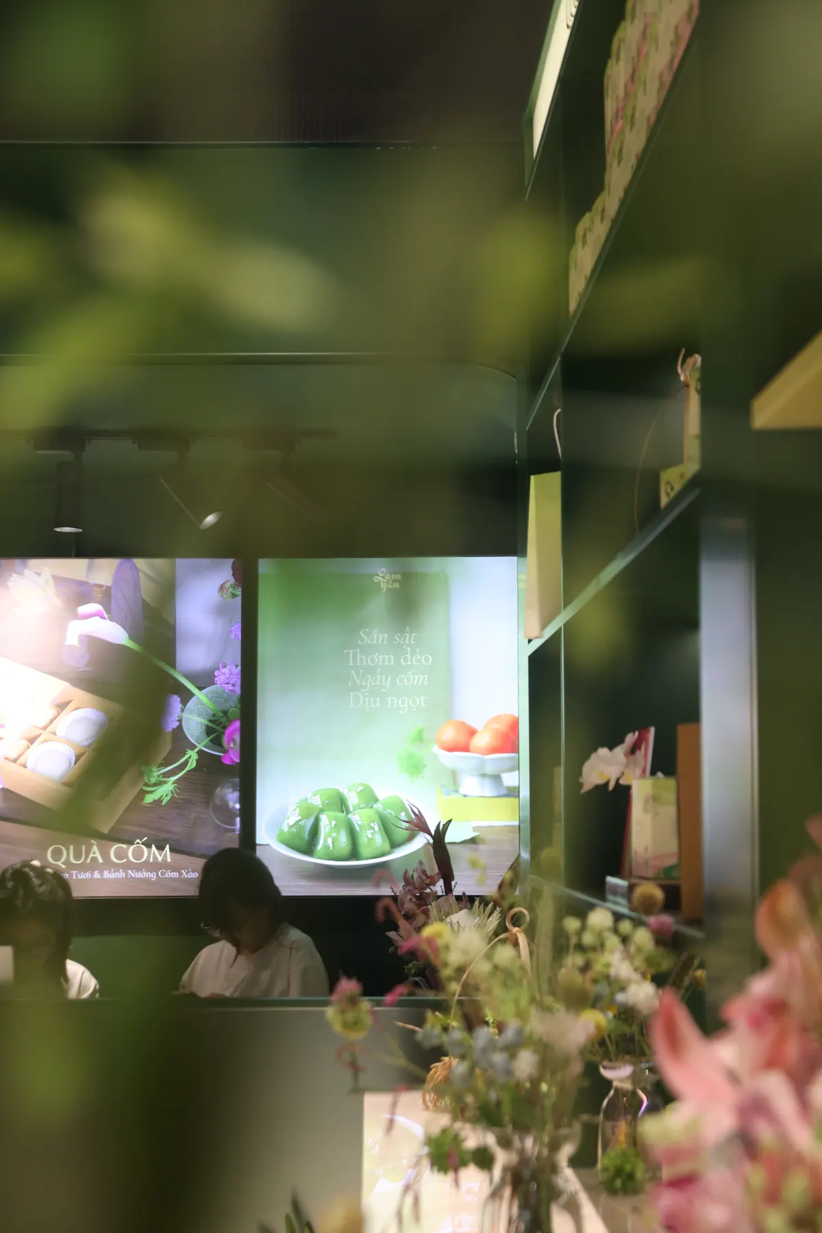 Inside the shop: flowers in the foreground and a screen showing cốm cakes.