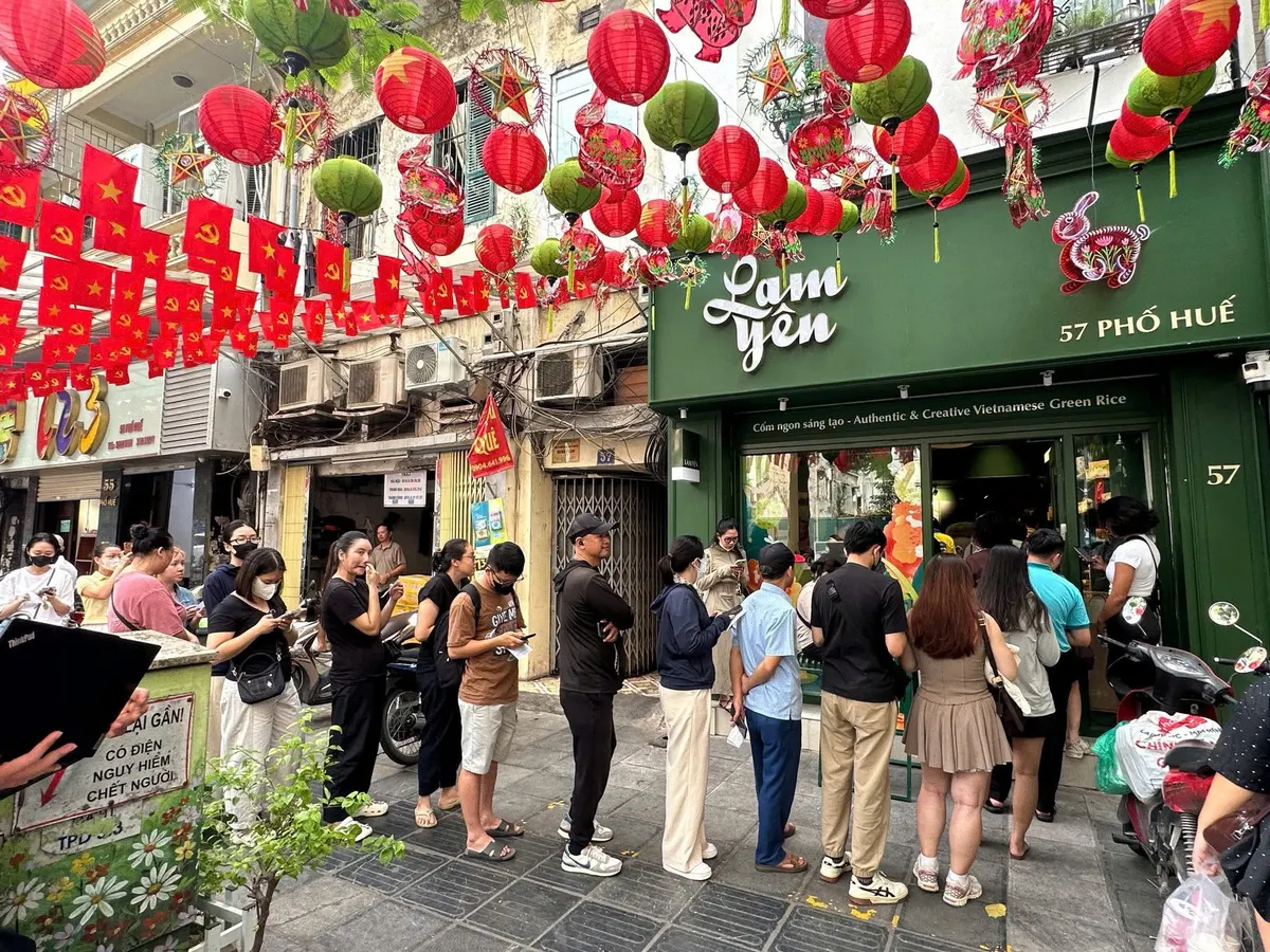 A line of customers along the street below red flags and lanterns outside the Lam Yên shop.