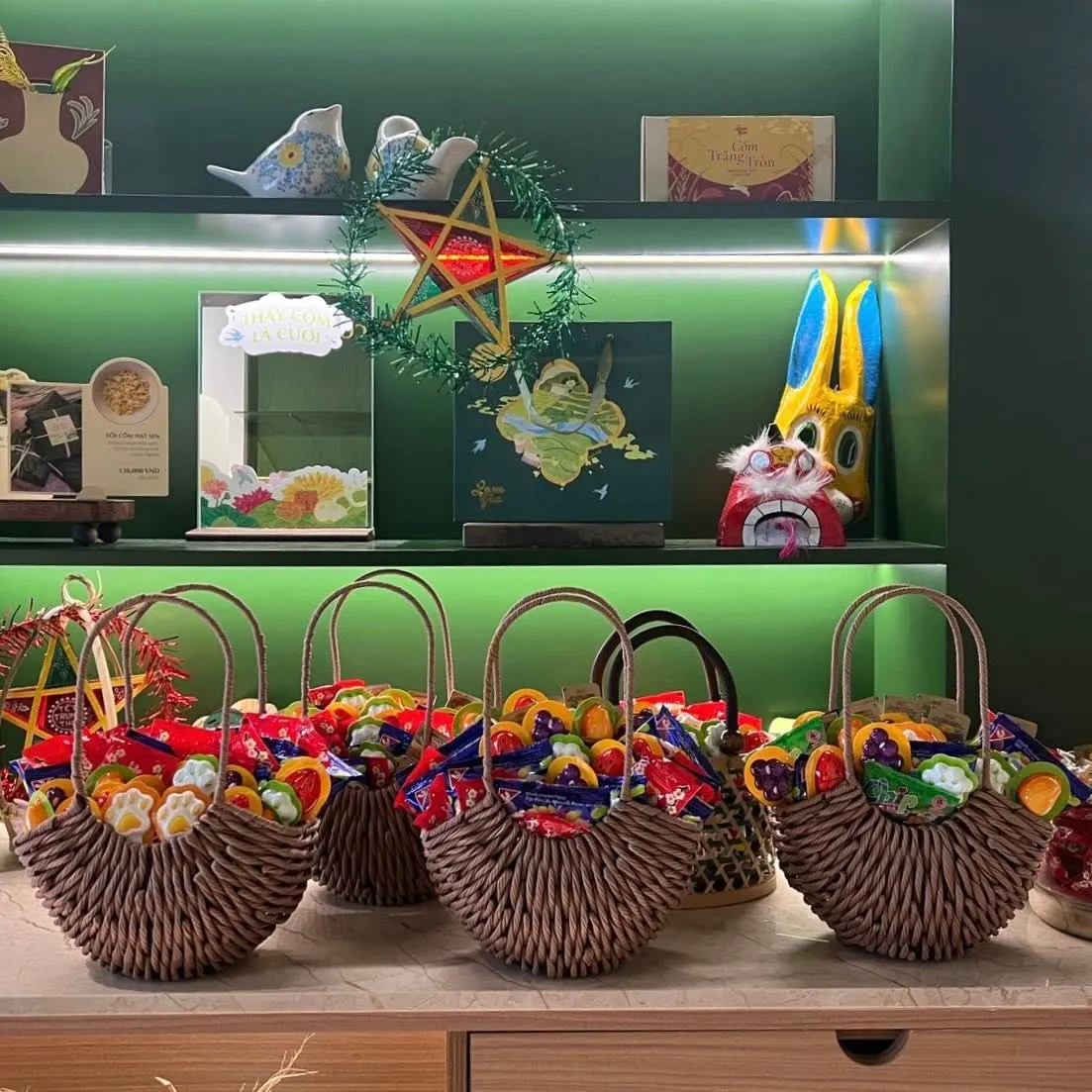 Woven baskets of festival lanterns and toys on a counter under a green shelf.