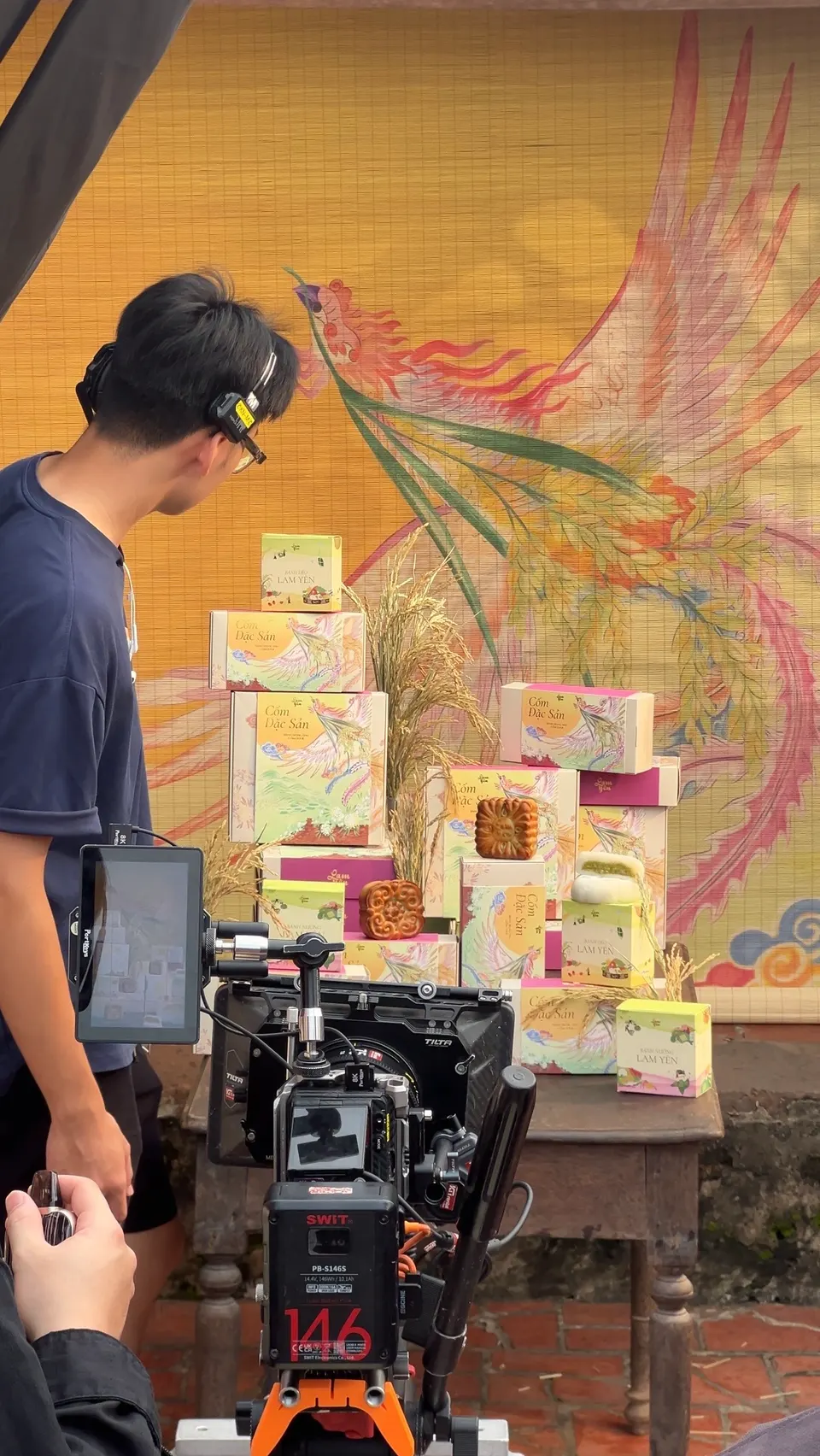A cameraman beside a set of stacked gift boxes in front of a painted phoenix backdrop.