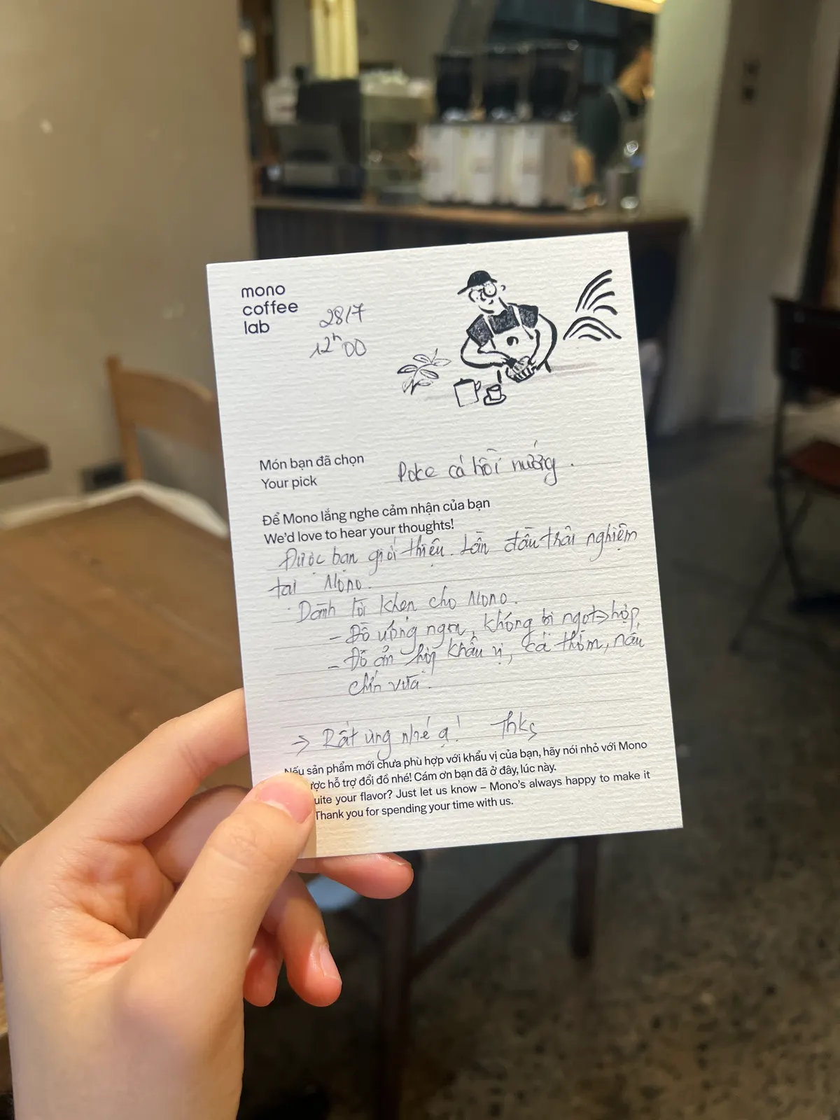 A hand holding up a Mono Coffee Lab guest opinion card, filled in by hand, in the café (card 5 of 9).