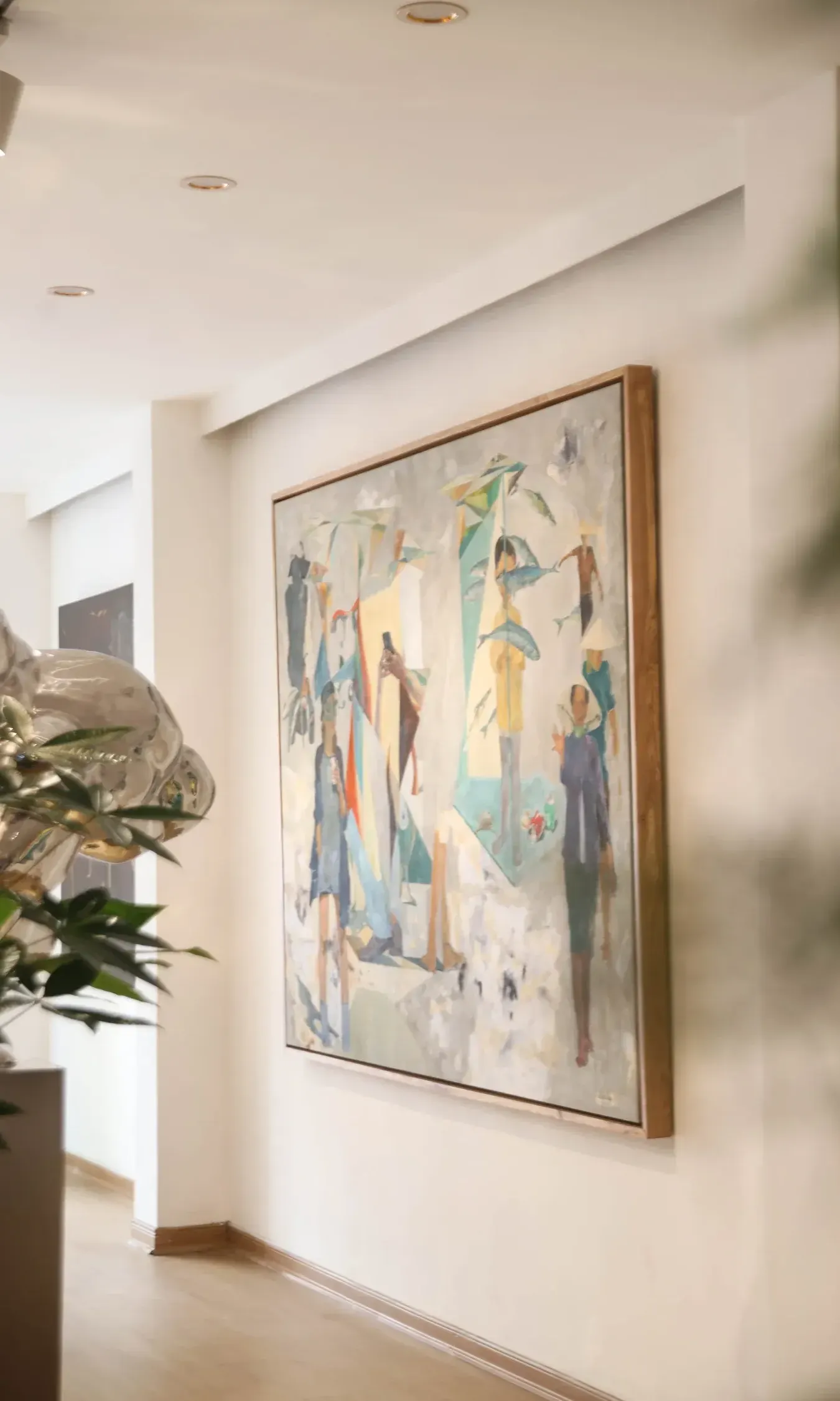 A framed painting of figures hanging on a sunlit gallery wall, a plant in the foreground.