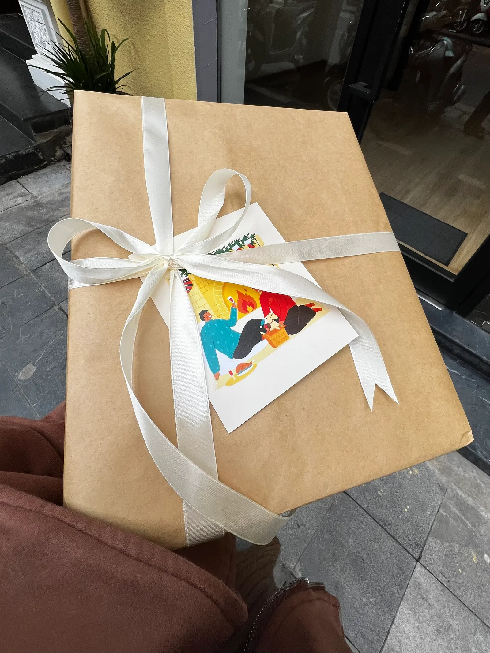 A parcel wrapped in kraft paper with a wide cream satin ribbon and an illustrated card.